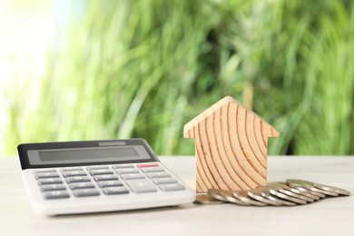 Photo of Wooden house model, calculator and coins on light table outdoors