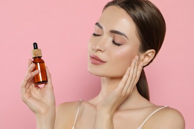 Photo of Young woman with bottle of essential oil on pink background