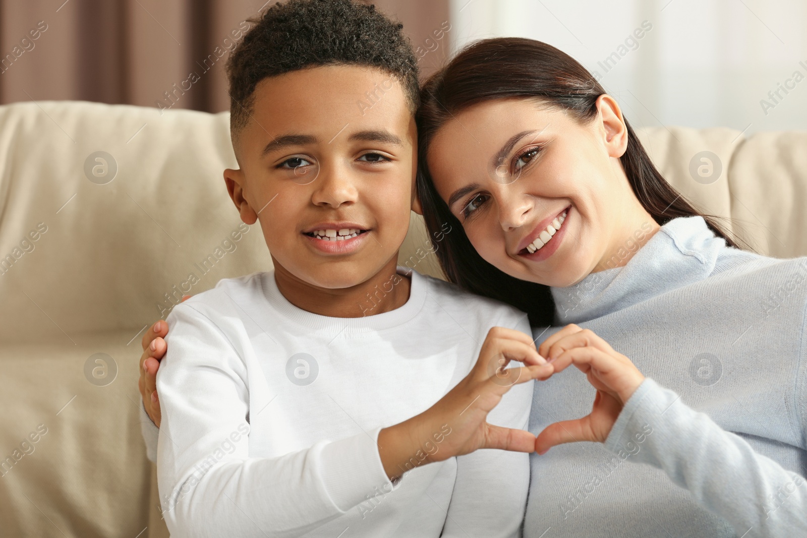 Photo of Mother and her African American son making heart with hands indoors. International family