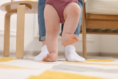 Photo of Mother supporting her baby son while he learning to walk on carpet at home, closeup