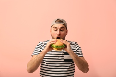 Photo of Young man eating tasty burger on color background