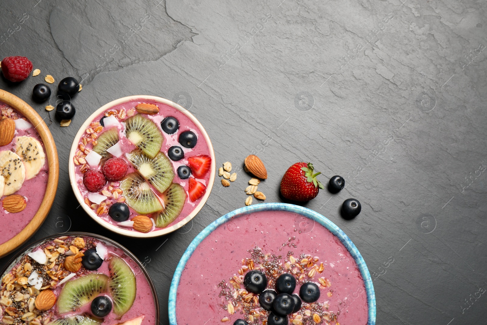 Photo of Acai smoothie bowls with granola and fruits on black table, flat lay. Space for text
