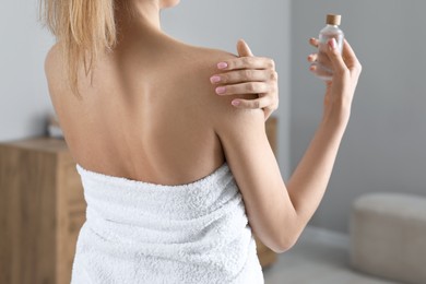 Woman applying body oil onto shoulder in bathroom, closeup