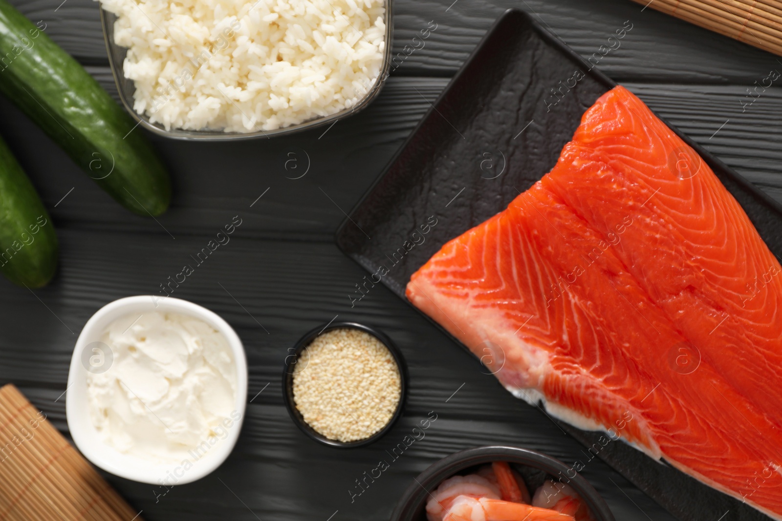 Photo of Making sushi rolls. Flat lay composition with ingredients on black wooden table