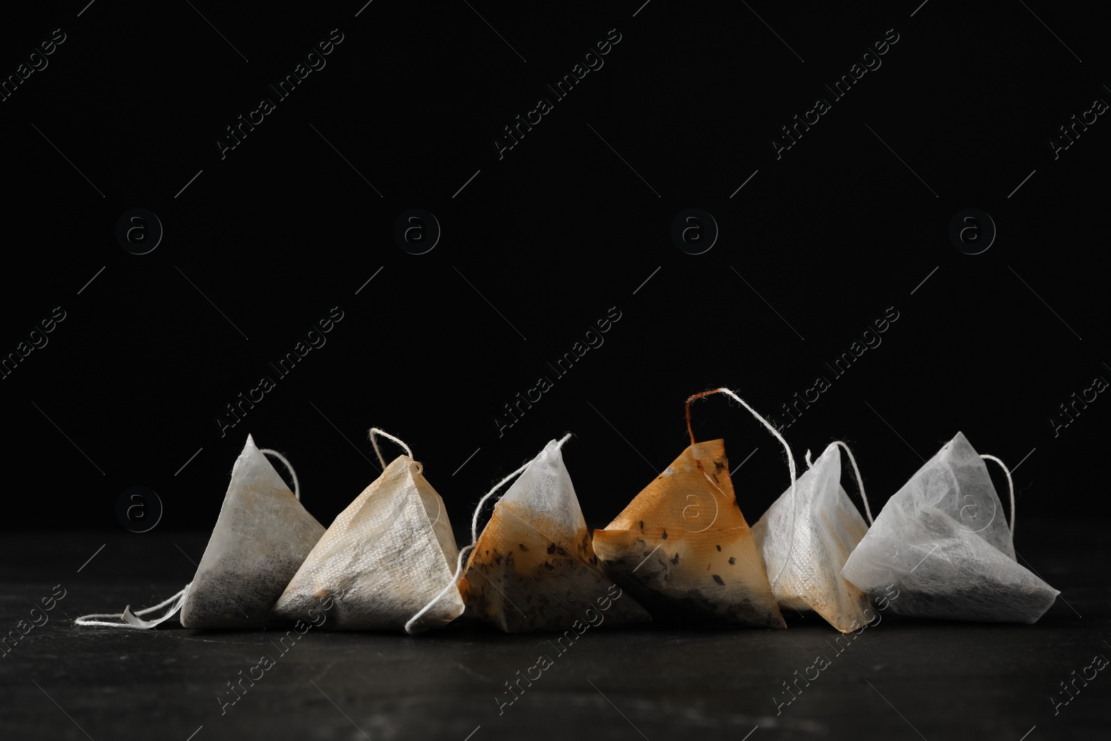 Photo of Pyramid tea bags on dark table against black background. Space for text