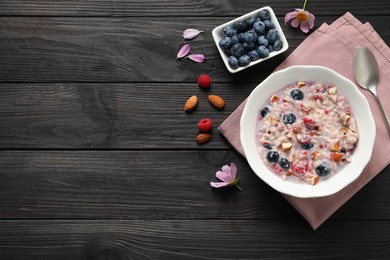 Photo of Tasty oatmeal porridge with toppings on black wooden table, flat lay. Space for text