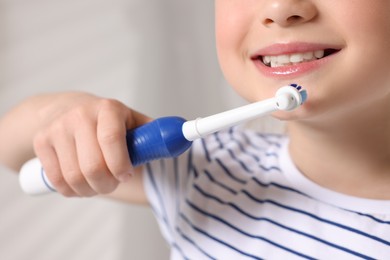 Photo of Little girl brushing her teeth with electric toothbrush on blurred background, closeup