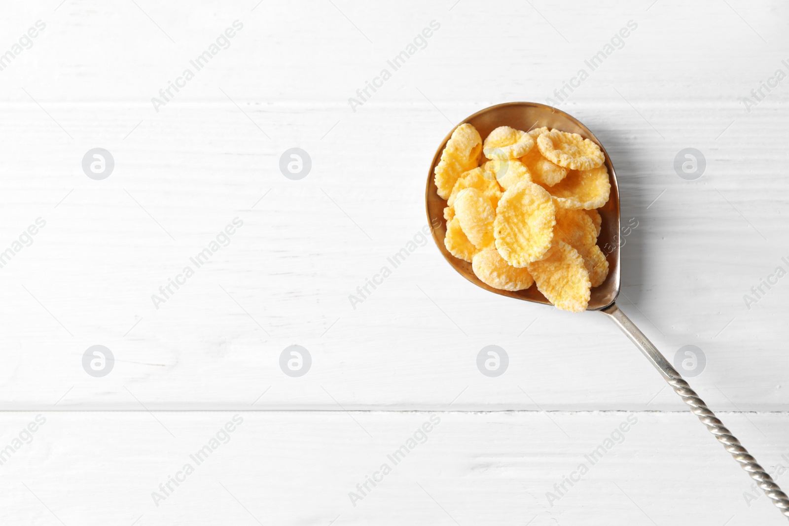 Photo of Metal spoon of tasty crispy corn flakes on white wooden table, top view. Space for text