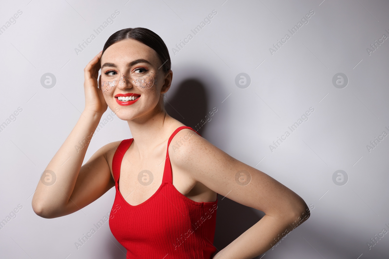 Photo of Happy woman with glitter freckles on light background. Space for text