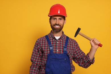 Photo of Professional builder in uniform with hammer on yellow background