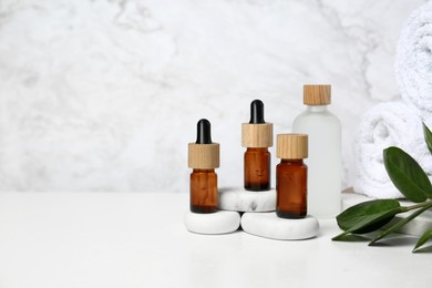 Bottles of essential oil, green leaves and spa stones on white table, space for text