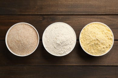 Photo of Different types of flours on bowls on wooden table, flat lay
