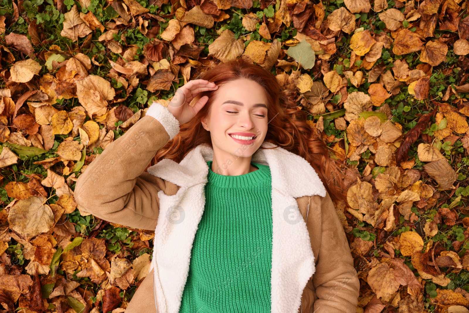 Photo of Smiling woman lying among autumn leaves outdoors, top view