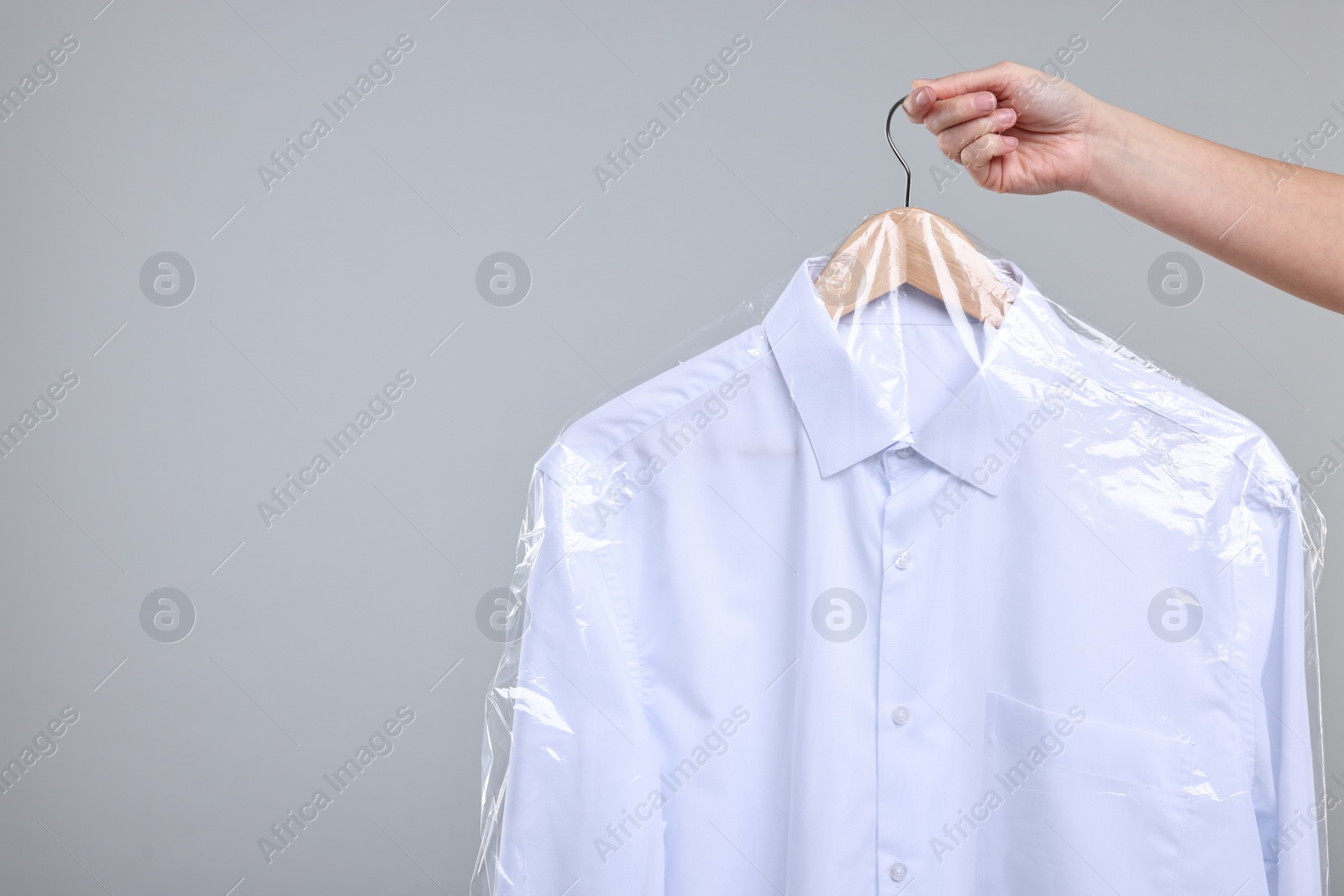 Photo of Dry-cleaning service. Woman holding shirt in plastic bag on gray background, closeup. Space for text