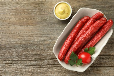 Photo of Thin dry smoked sausages served with sauce on old wooden table, flat lay. Space for text