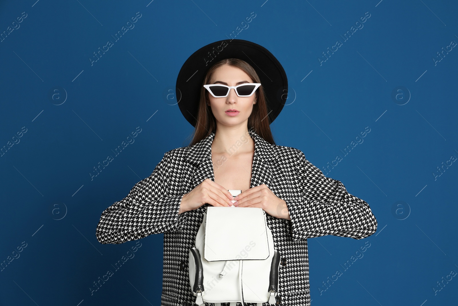 Photo of Beautiful young woman in sunglasses with stylish bag on blue background