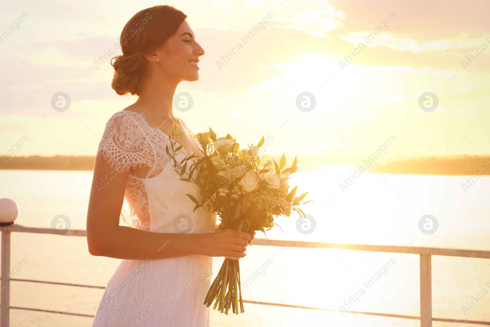 Photo of Gorgeous bride in beautiful wedding dress with bouquet near river on sunset