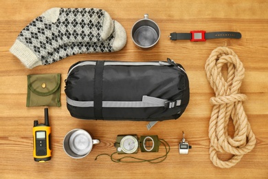 Flat lay composition with sleeping bag and camping equipment on wooden background