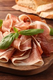 Photo of Slices of tasty cured ham and basil on wooden board, closeup