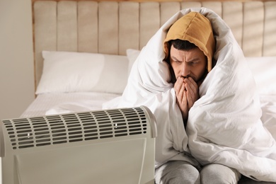 Photo of Man sitting in bed near electric heater at home