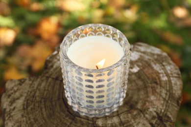 Burning candle on wooden surface outdoors, closeup. Autumn atmosphere