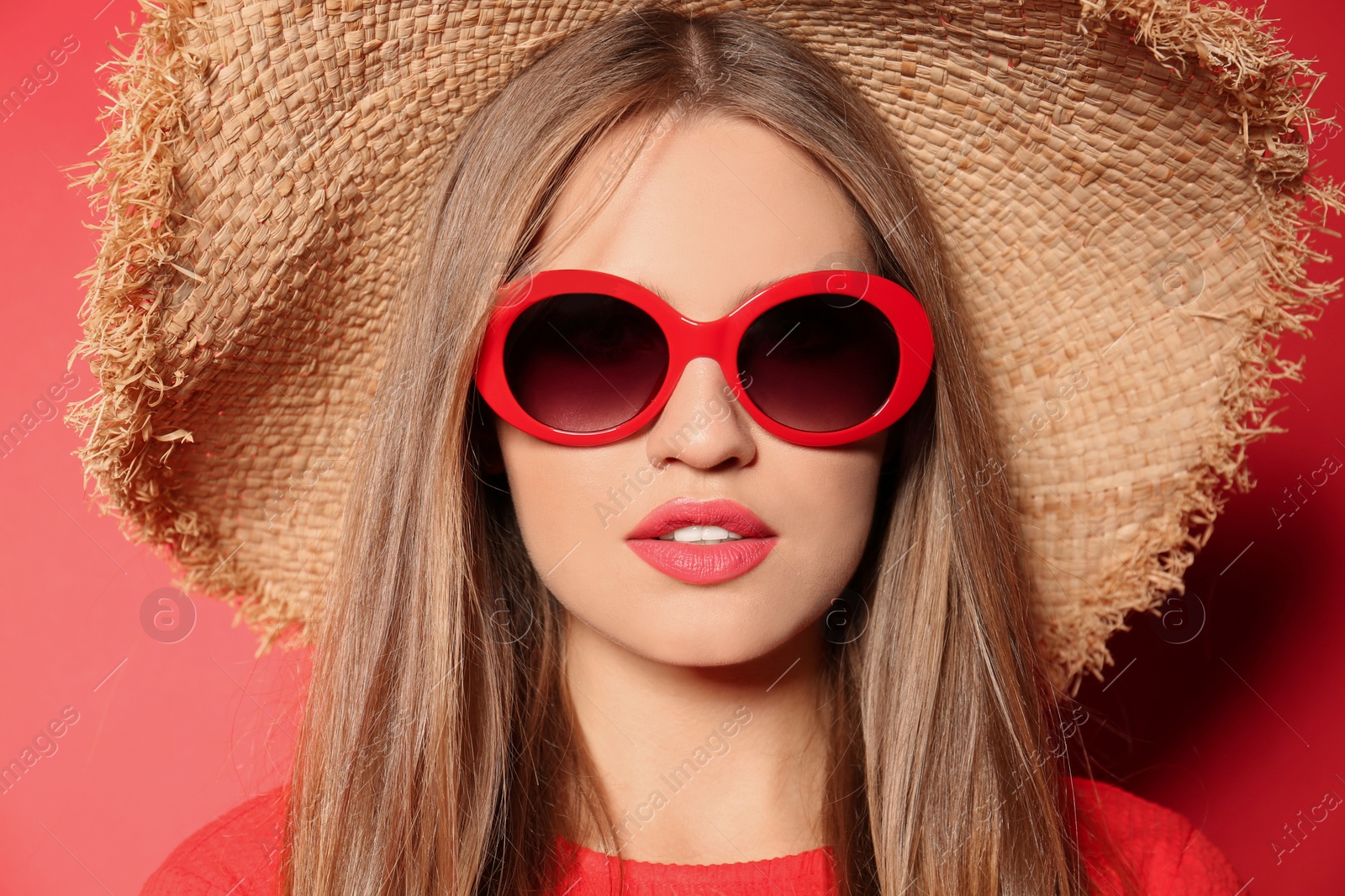 Photo of Young woman wearing stylish sunglasses and hat on red background