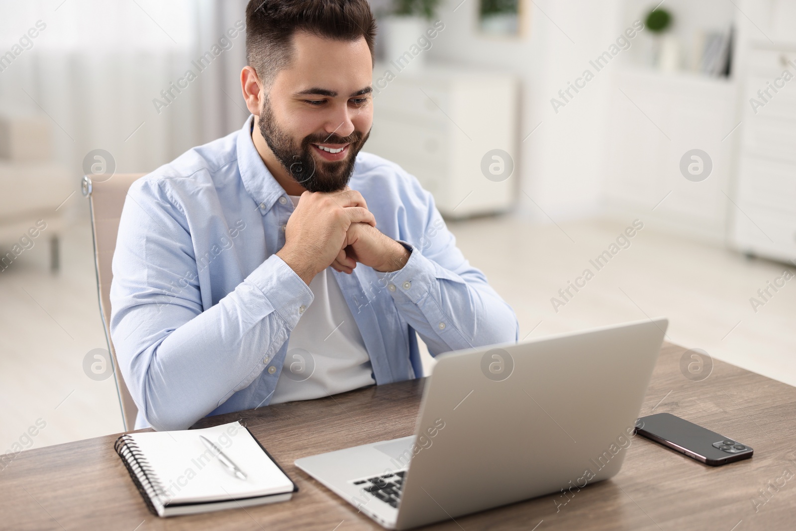 Photo of Young man watching webinar at table in room