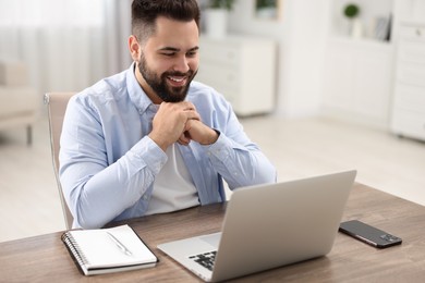 Young man watching webinar at table in room