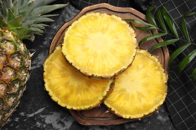 Photo of Slices of tasty ripe pineapple on black textured table, flat lay