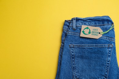 Photo of Jeans with recycling label on yellow background, top view. Space for text