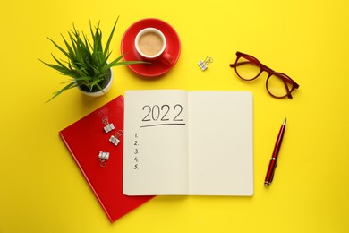 Photo of Flat lay composition with open planner on yellow background. 2022 New Year aims