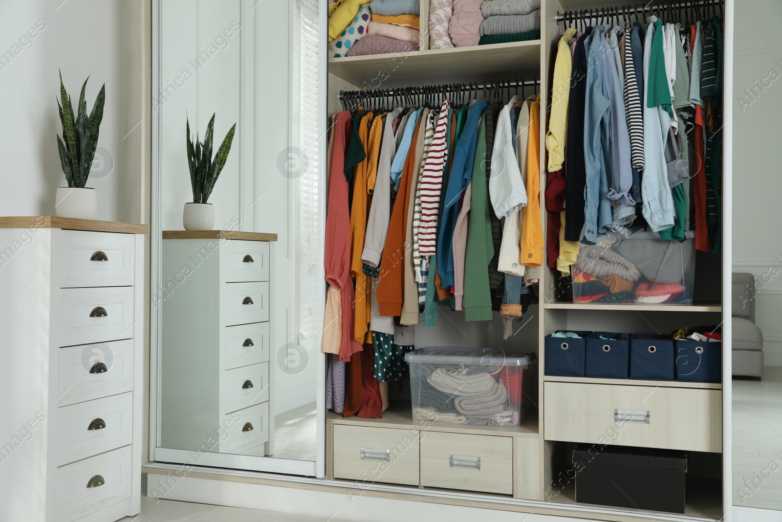 Photo of Wardrobe closet with different stylish clothes and home stuff in room. Fast fashion