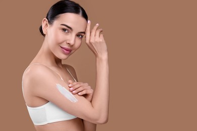 Photo of Beautiful woman with smear of body cream on her arm against light brown background, space for text