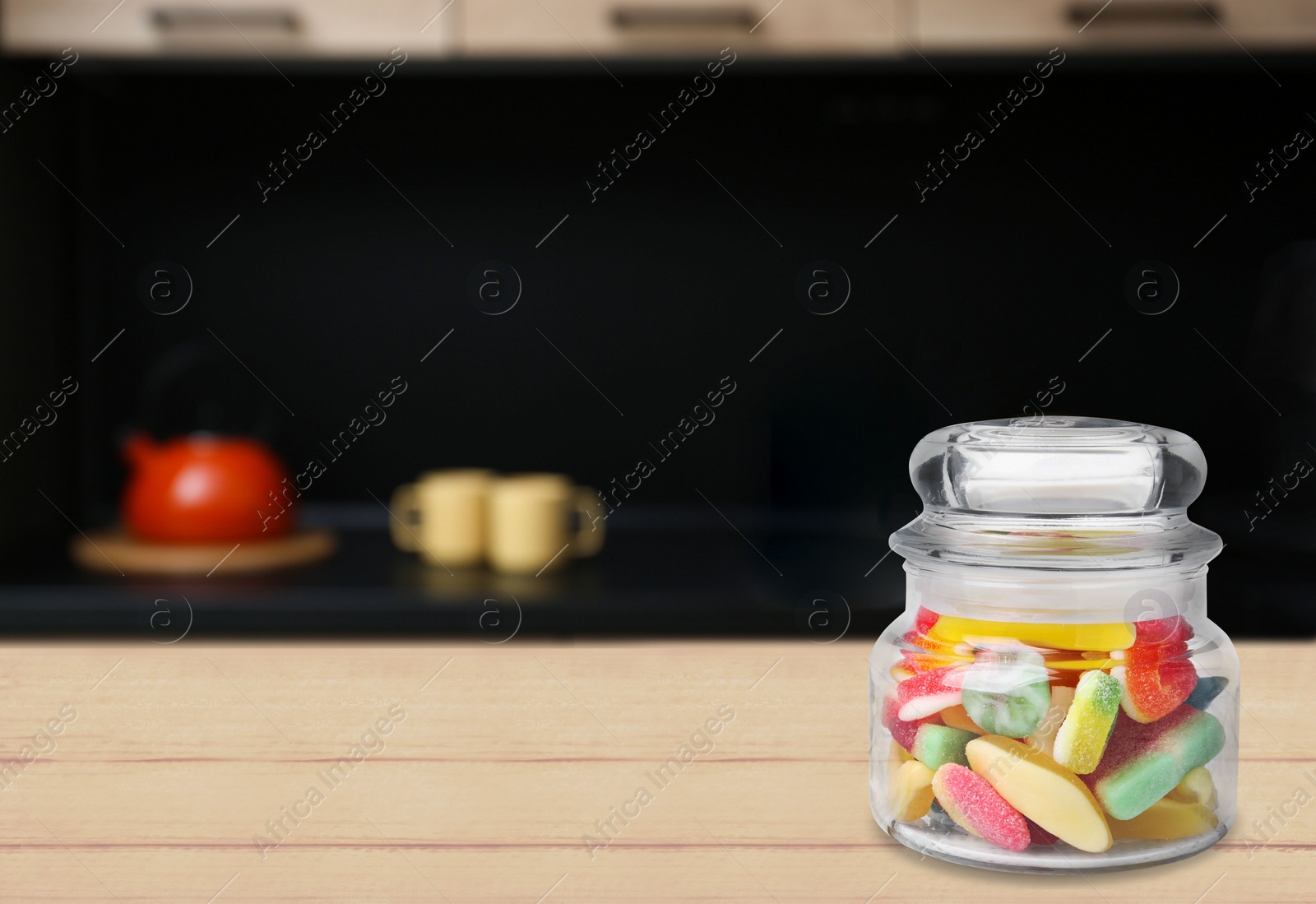 Image of Glass jar with tasty gummy candies on wooden table in kitchen. Space for text