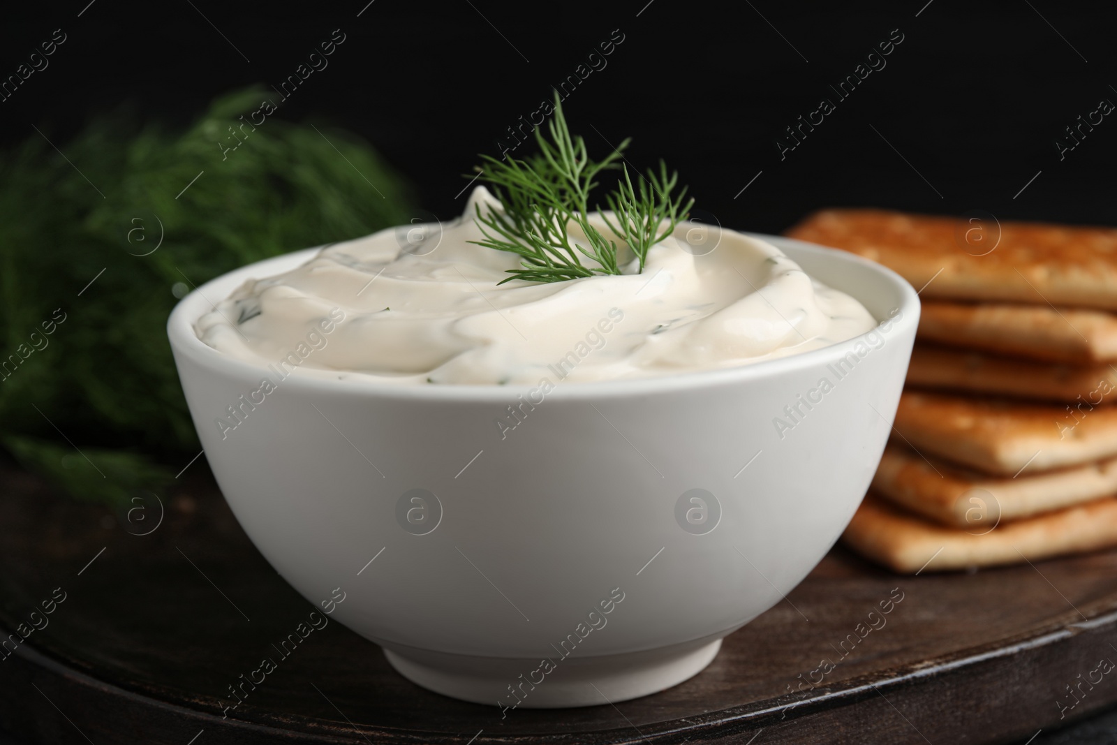 Photo of Tasty creamy dill sauce in bowl on wooden board, closeup