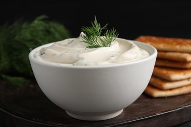 Photo of Tasty creamy dill sauce in bowl on wooden board, closeup