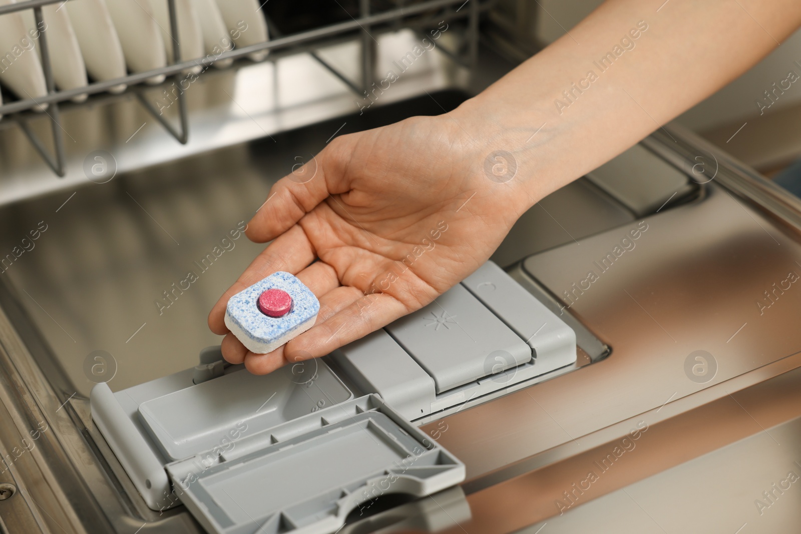 Photo of Woman putting detergent tablet into open dishwasher, closeup