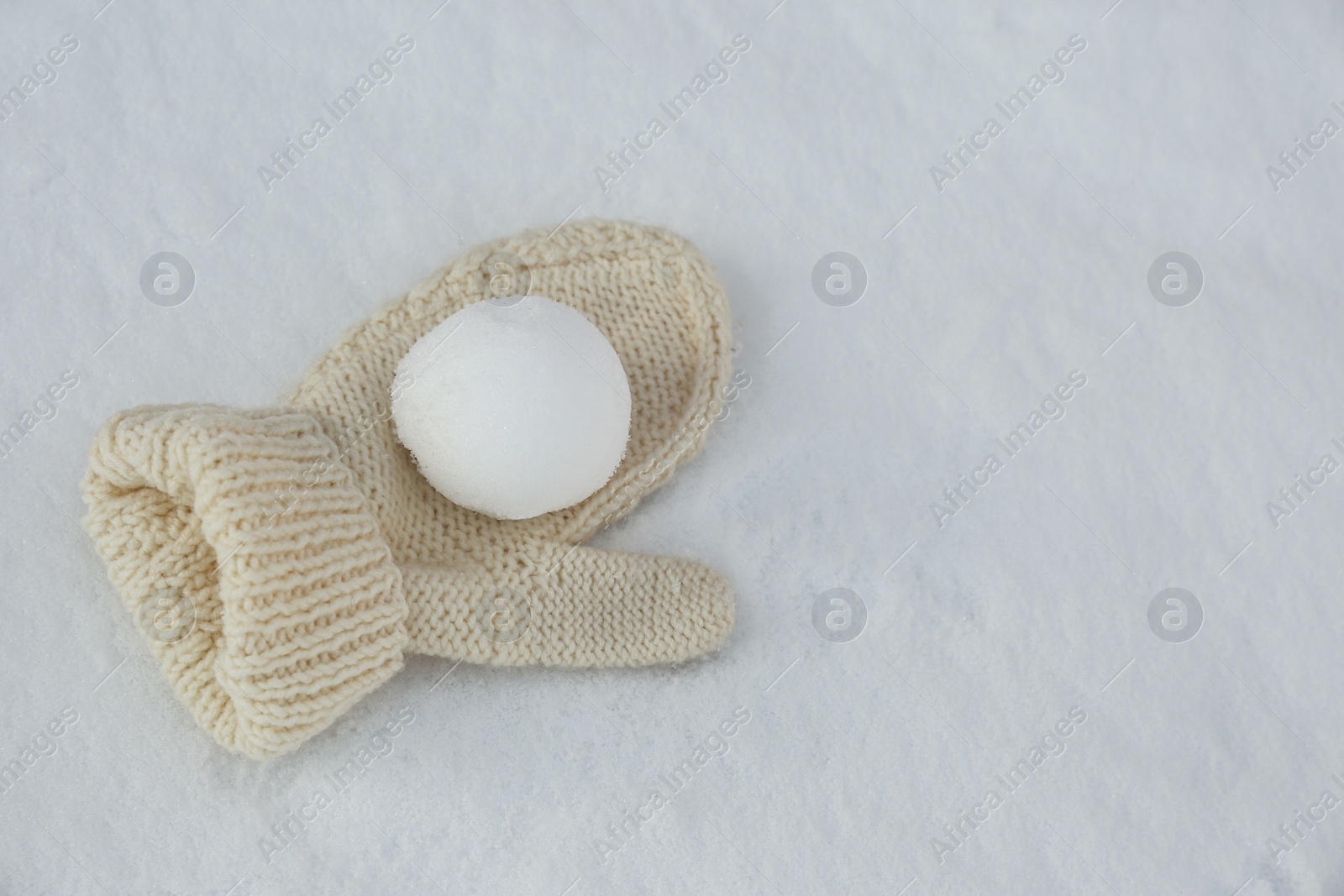 Photo of Knitted mitten and snowball on snow outdoors. Space for text