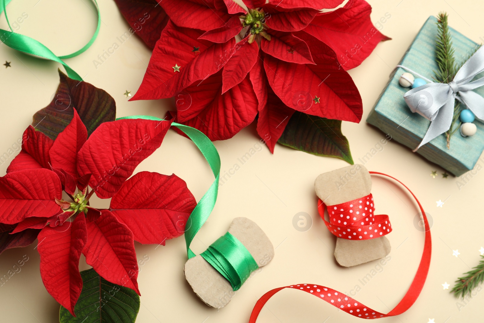 Photo of Flat lay composition with poinsettias (traditional Christmas flowers) and holiday decor on beige background