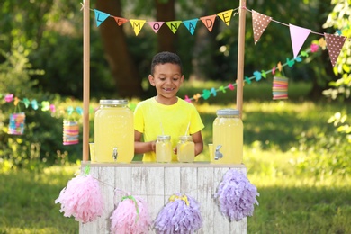Photo of Cute little African-American boy at lemonade stand in park. Summer refreshing natural drink