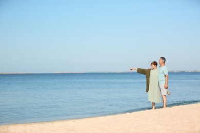 Happy mature couple walking at beach on sunny day