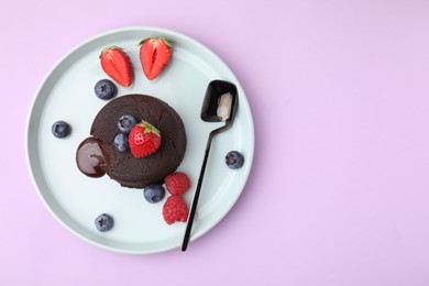 Photo of Plate with delicious chocolate fondant and berries on violet table, top view. Space for text