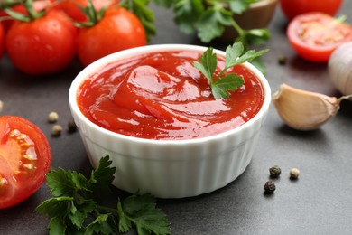 Delicious ketchup in bowl, tomatoes, parsley and garlic on grey table, closeup