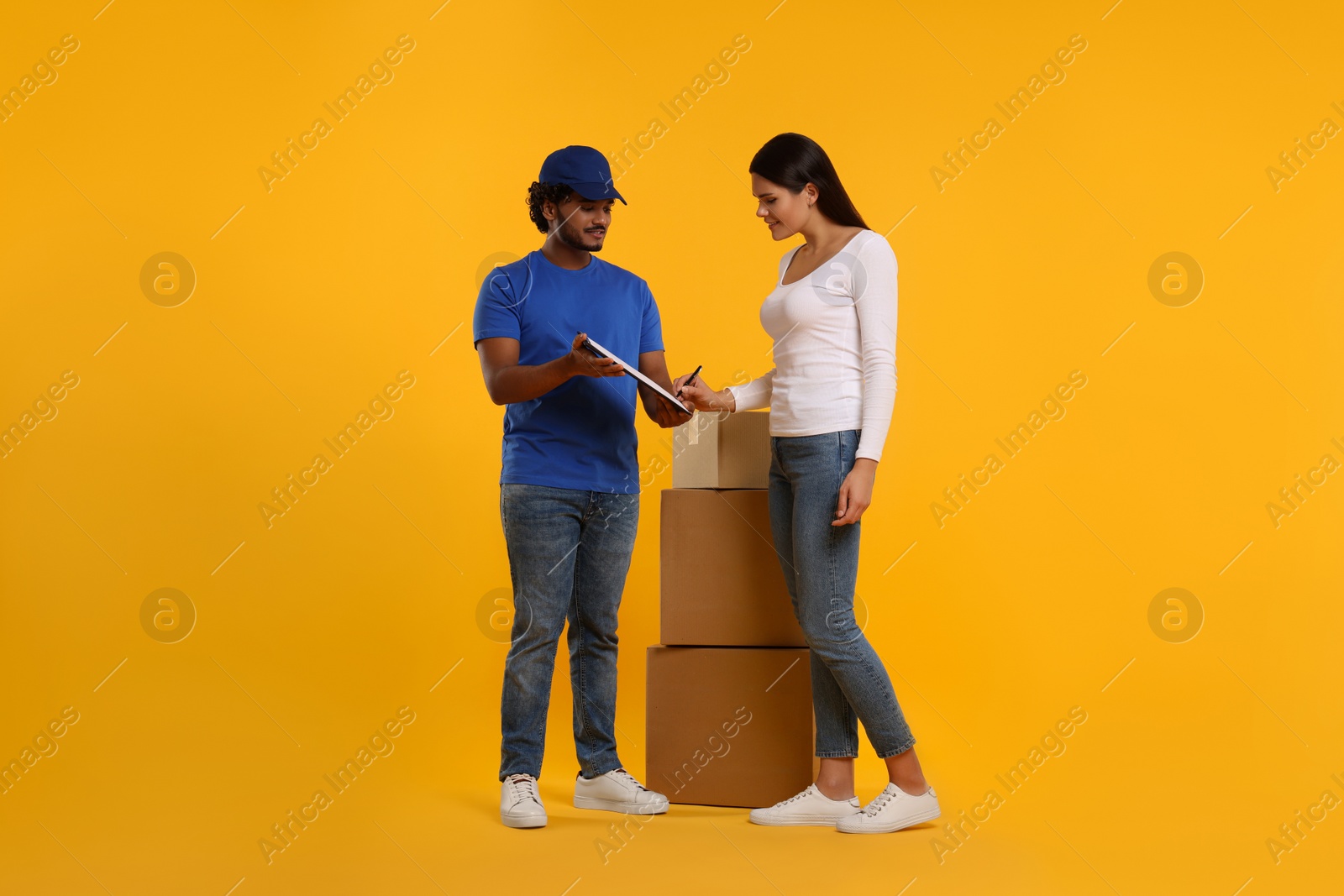 Photo of Happy young woman signing order receipt on orange background. Courier delivery