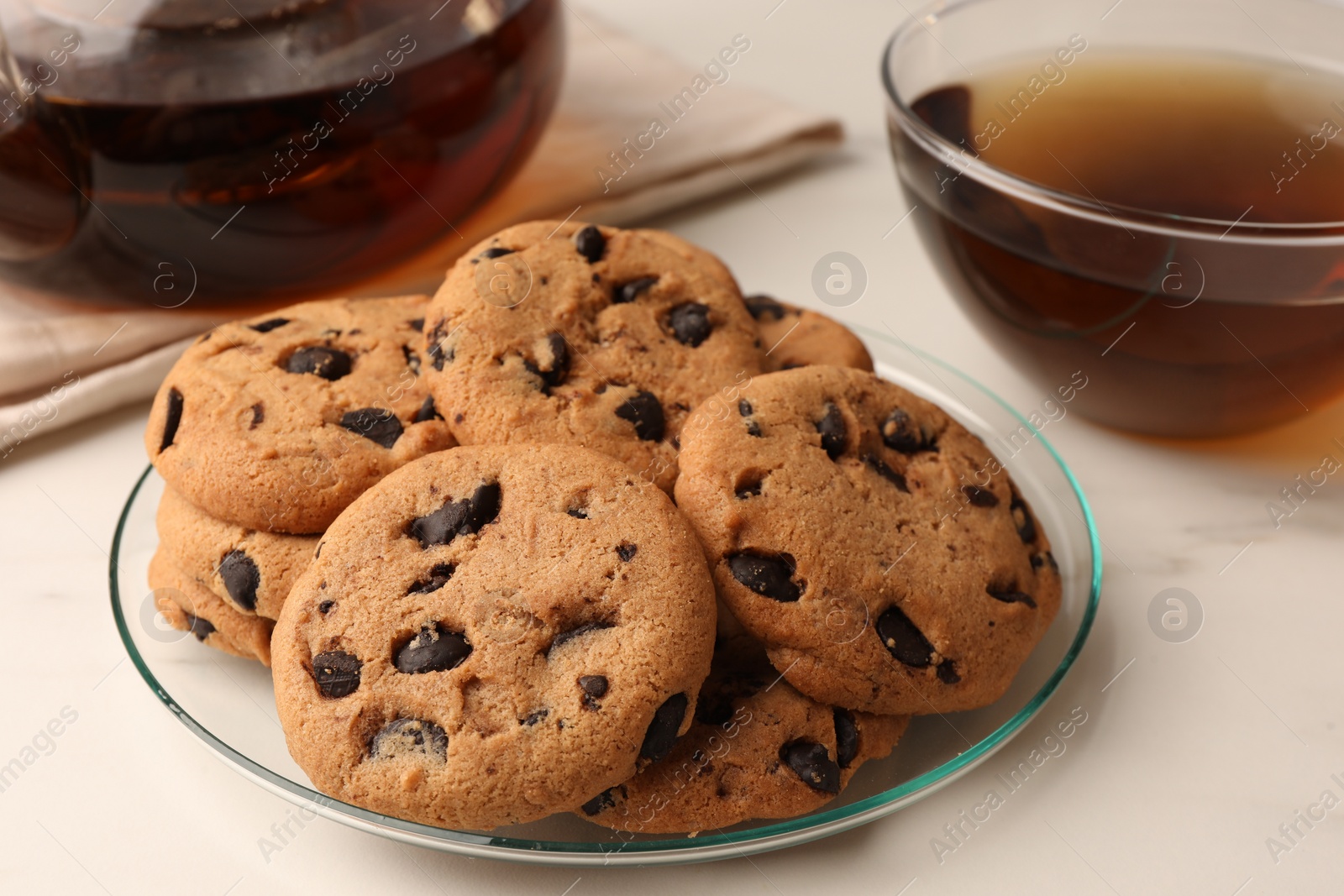 Photo of Delicious chocolate chip cookies and tea on white marble table, closeup