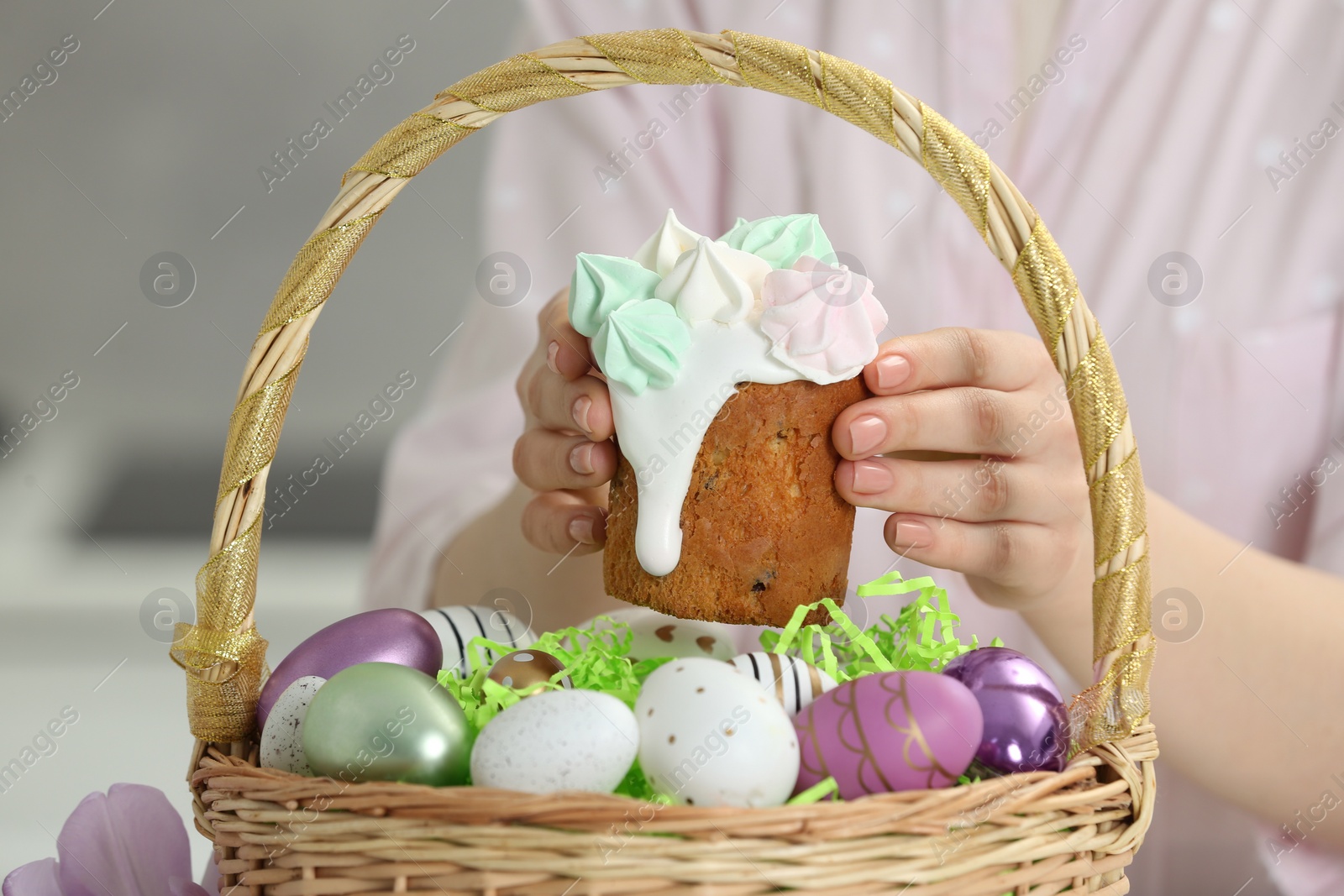 Photo of Woman putting delicious Easter cake with meringues into wicker basket with colorful eggs, closeup