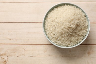 Photo of Raw basmati rice in bowl on white wooden table, top view. Space for text