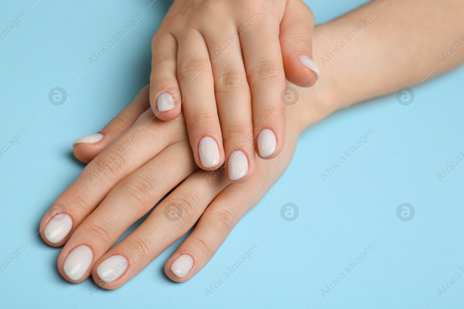 Photo of Woman showing her manicured hands with white nail polish on light blue background, closeup