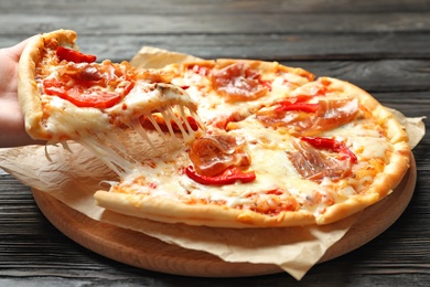 Photo of Woman holding slice of delicious hot pizza over table, closeup