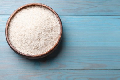 Photo of Raw basmati rice in bowl on light blue wooden table, top view. Space for text